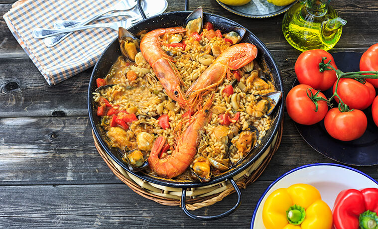 Paella in a pan with prawns on top and fresh tomatoes and peppers on the table nearby