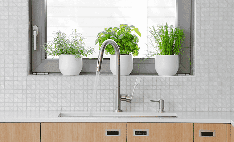Water gushes from an elegant stainless steel tap into the sink in a modern kitchen with a stone bench and white mosaictiled splashback
