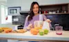 Young woman in a purple jumper juices oranges in a food processor at home