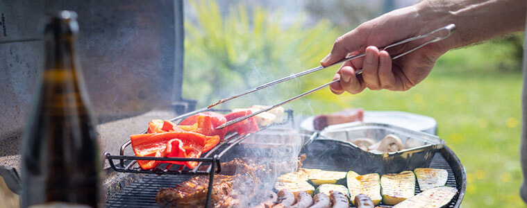 A man cooks sausages steak and vegetables on an outdoor grill in his backyard