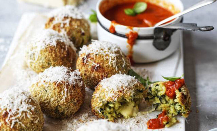 Spinach  mozzarella arancini with roast tomato sauce on a rectangular white plate