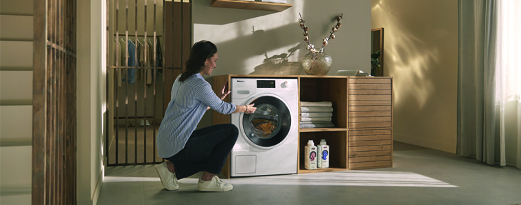 A woman uses her Miele washing machine in a light and airy laundry