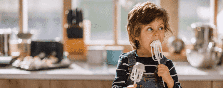 Child licking whisk in kitchen