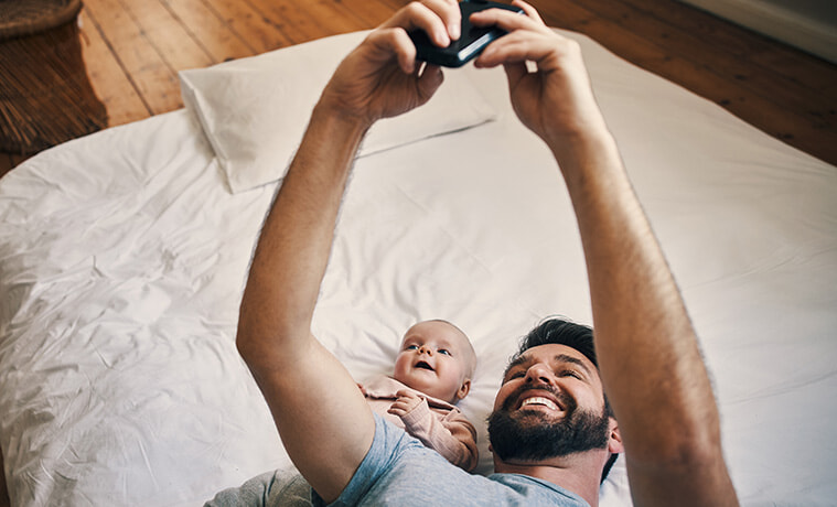 High angle shot of an affectionate young father taking selfies with his baby girl while lying on a bed at home