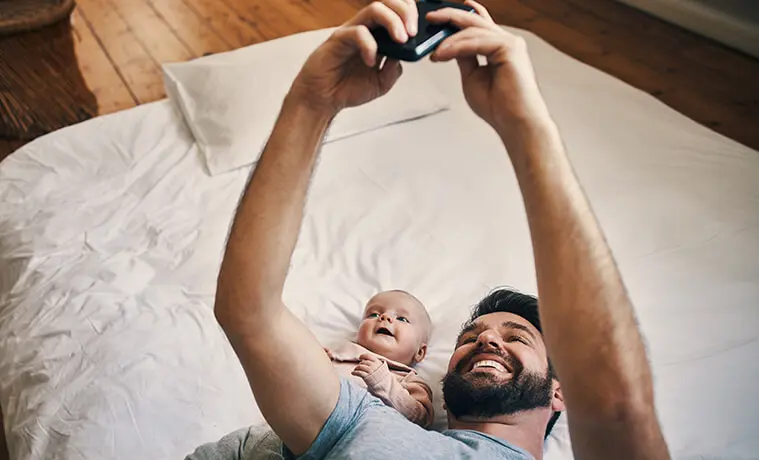 High angle shot of an affectionate young father taking selfies with his baby girl while lying on a bed at home
