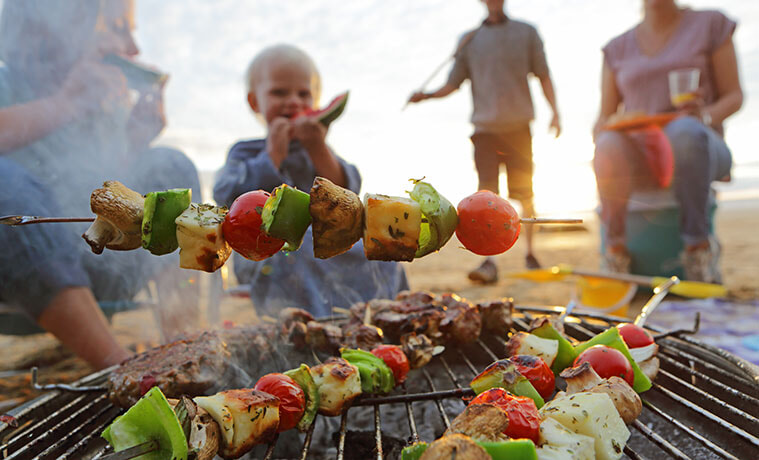 Family enjoying vegetable and haloumi skewers at a barbecue on the beach