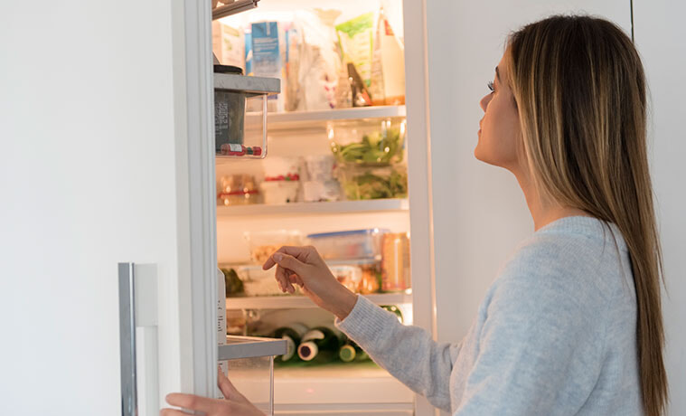 A woman opens the door of her integrated fridge and looks inside 