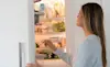 A woman opens the door of her integrated fridge and looks inside 