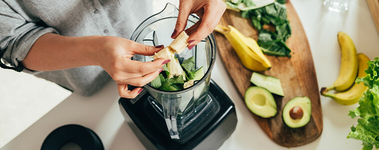 A woman prepares a healthy detox drink in a blender using fresh fruits spinach and avocado