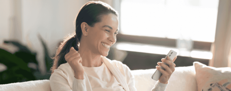a woman sitting on her couch looking at her phone excitedly 