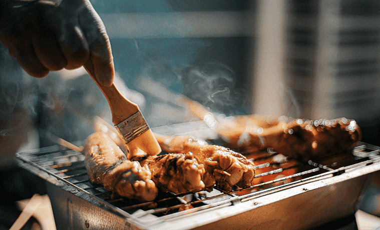 Closeup of a man basting marinated chicken skewers on a grill