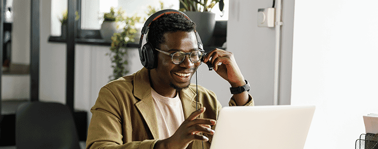 A man wearing a suit jacket and headphones chats to a colleague in an online meeting on his laptop