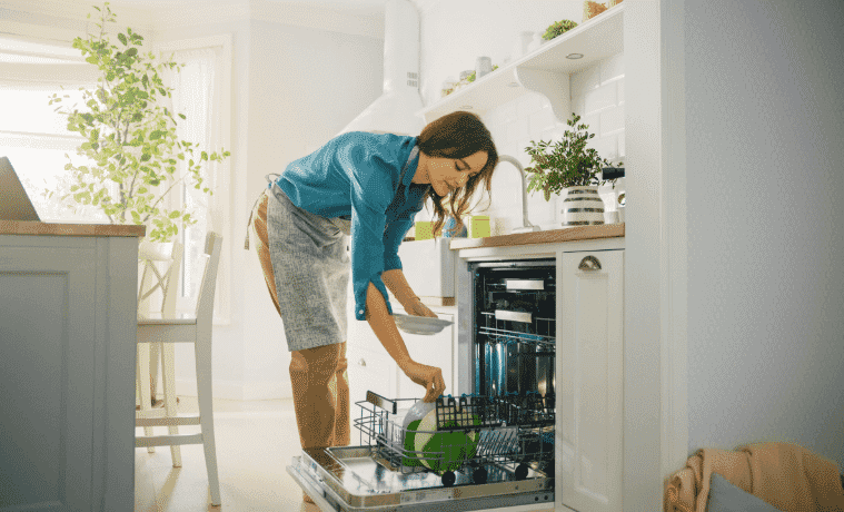 A woman loads the dishwasher in her kitchen