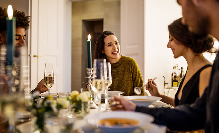 Smiling young woman talking with friends while having dinner at home