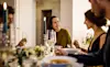 Smiling young woman talking with friends while having dinner at home