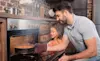 Man pulls out cooking from his new steam oven whilst his daughter smiles and looks on