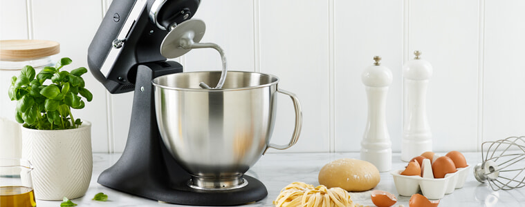 A matt black KitchenAid Artisan Stand Mixer sits in a white modern kitchen on a grey benchtop