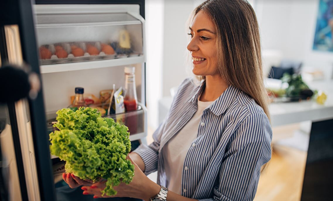 A woman removes a head of lettuce from her fridge