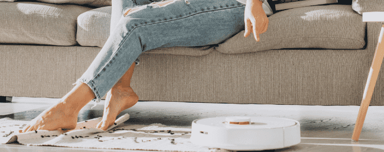 Robot vacuum cleans the lounge room as a lady relaxes on the couch