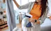 A woman holds a handheld garment steamer up to her striped shirt on a hanger to remove the creases
