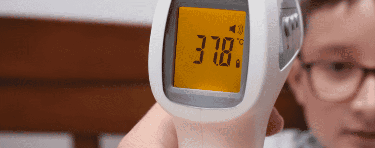 A person holds a digital thermometer to a childs forehead
