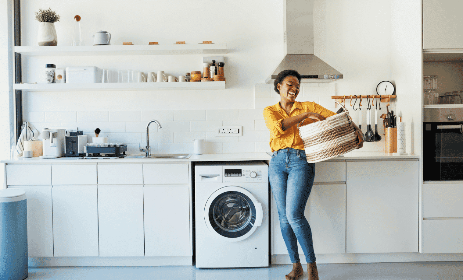 A woman brings a basket of clothing into her white laundry