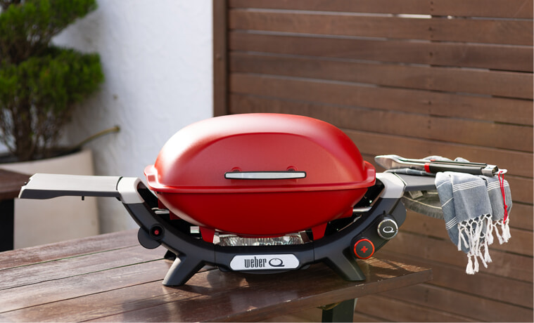 A red Weber Q sits on a table on a deck in a backyard