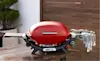 A red Weber Q sits on a table on a deck in a backyard