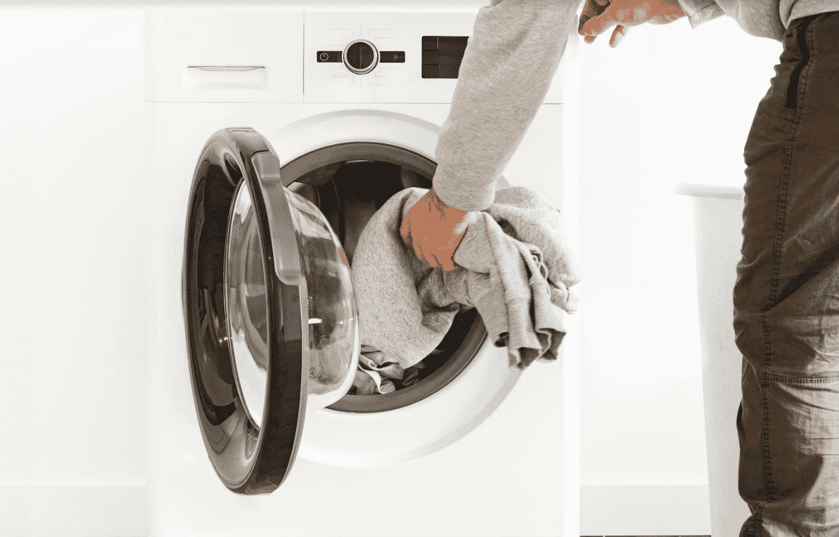 Closeup of a woman placing a grey knitted jumper in her washing machine
