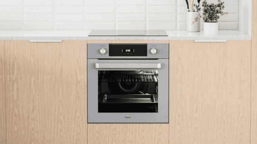 A chrome quad door Haier fridge sits in a modern kitchen with the top doors open displaying the fridges capacity 