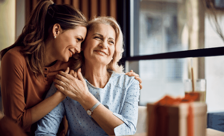 A woman and her daughter embrace with a present sitting on the table in front of them