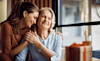 A woman and her daughter embrace with a present sitting on the table in front of them