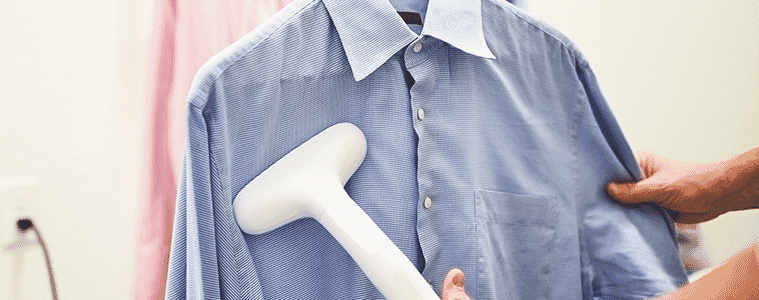 A closeup of a woman using a portable garment steamer on a linen shirt on a hanger 