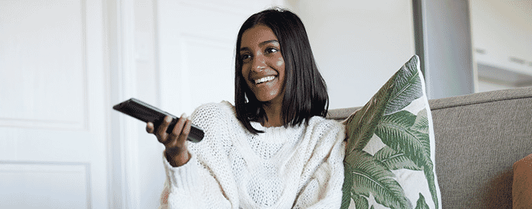 Woman with a TV remote smiling as she watches one of her favourite shows