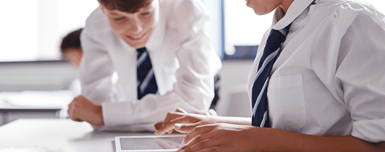 Two high school students in uniform complete a task on a tablet while in the classroom