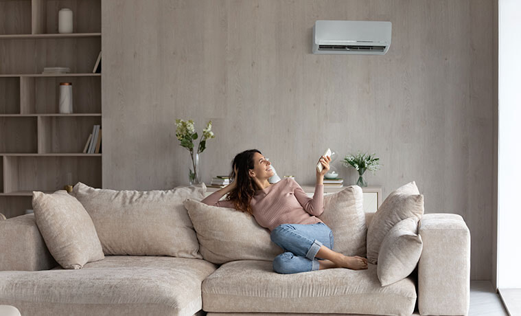 Relaxed woman turns on the air conditioning with a remote control from her couch