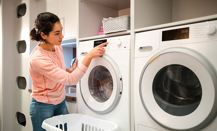 Young woman selects a program on a white washing machine in a home laundry 