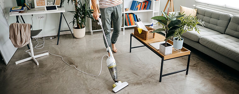 A man cleans the floor of his apartment using a stick vacuum cleaner