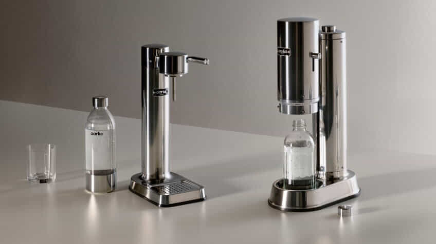 The aarke carbonator 3 and carbonator pro side by side on a modern kitchen bench surrounded by aarke bottles