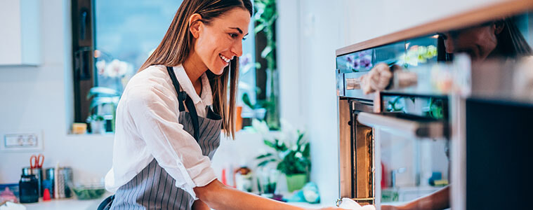 Woman removes a cooking tray from the wall oven in her modern kitchen