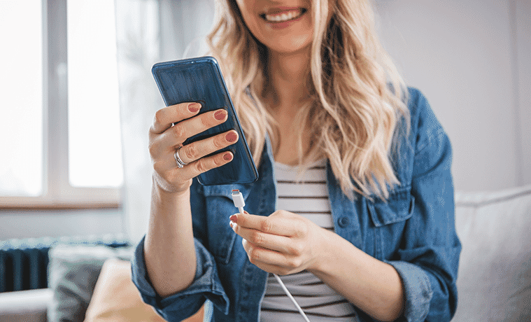 Woman plugs the charger into her smartphone while standing in her living room