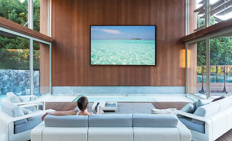 Woman watches a flat screen TV mounted on a living room wall 