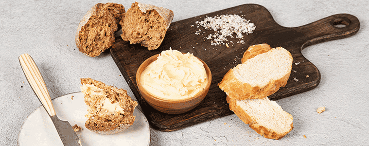 Bread rolls butter in a white bowl pile of salt and a knife on a brown chopping board on a grey table background