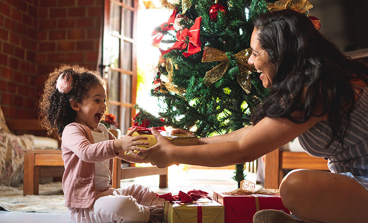 An excited young girl gives her mother a gift on Christmas morning 