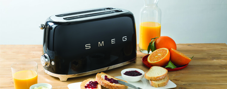 A black toaster surrounded by breakfast food on a light butchers block benchtop