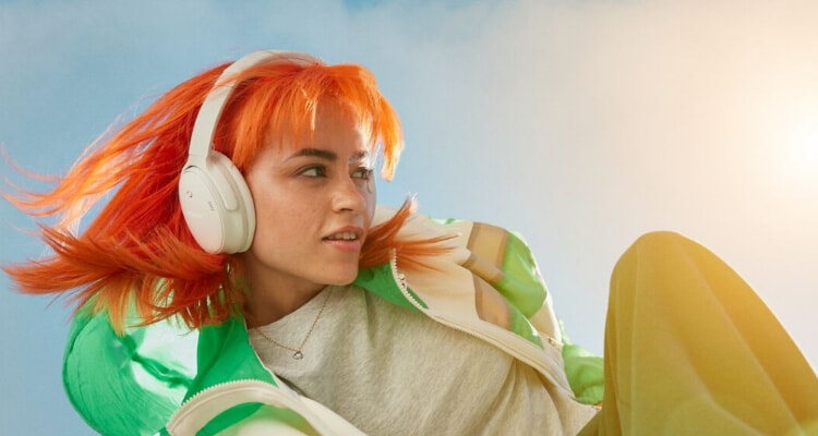 A woman with bright orange hair wears the Bose QuietComfort Headphones in white.