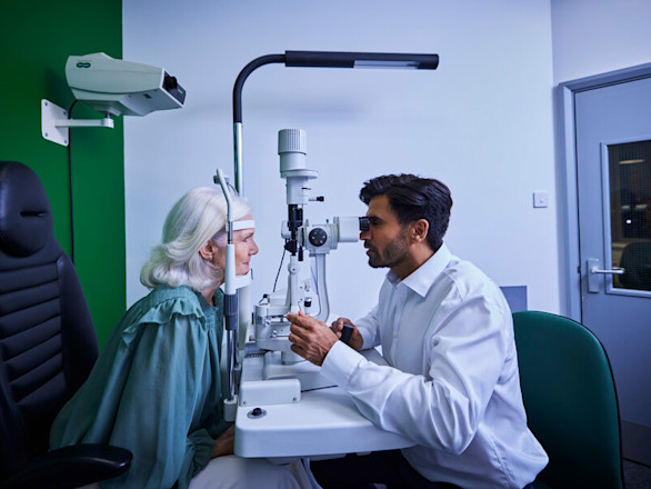 An older lady having her eyes tested by a man with black hair and a beard.