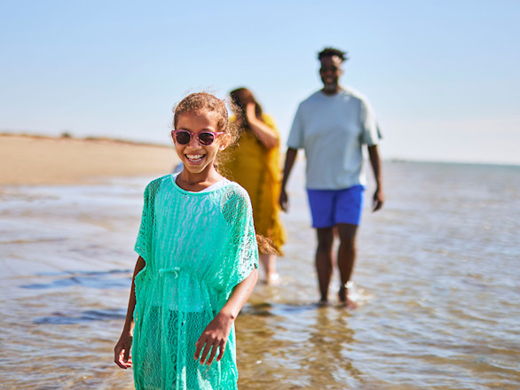 A girl in a green dress and sunglasses on the beach with family