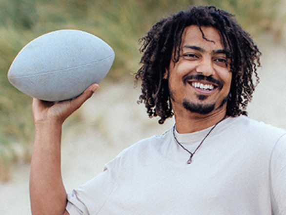 A young man playing with an American football on the beach