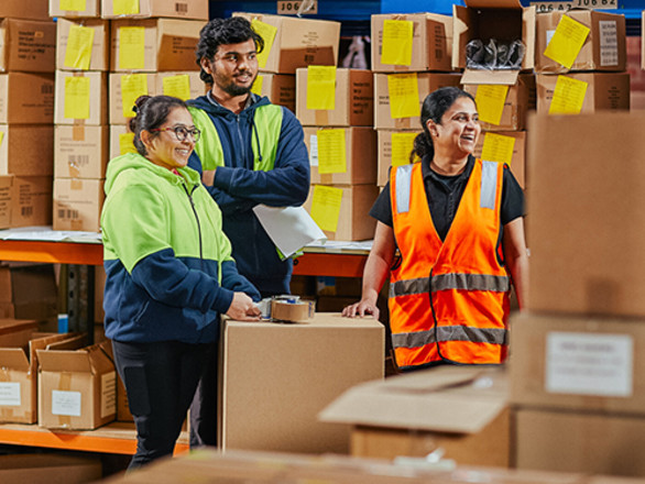 Three employees in hi-vis working in a warehouse surrounded by cardboard boxes.